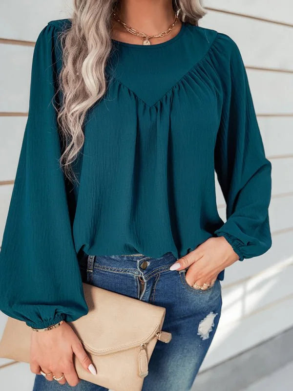 Teal textured long-sleeve peasant top with a gathered neckline, worn by a model with blue jeans and a light tan clutch.