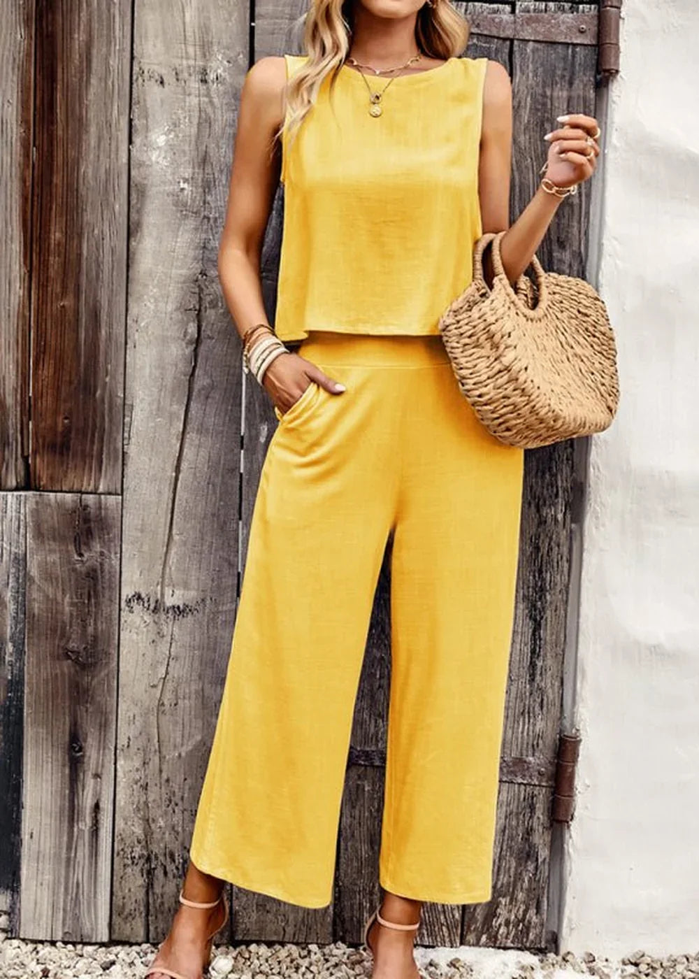 Yellow wide-leg pant suit with a sleeveless crop top, worn by a model with a straw bag and sandals.