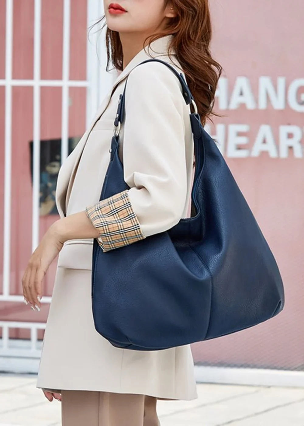 Navy blue leather tote bag with plaid interior trim, worn by a woman in a cream blazer.