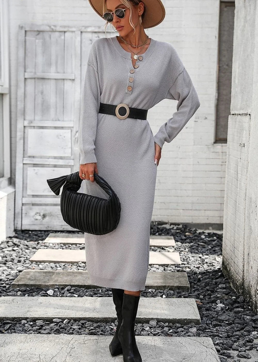 Light grey knit sweater dress with button detail, cinched waist belt, black pleated handbag, and black boots on model.