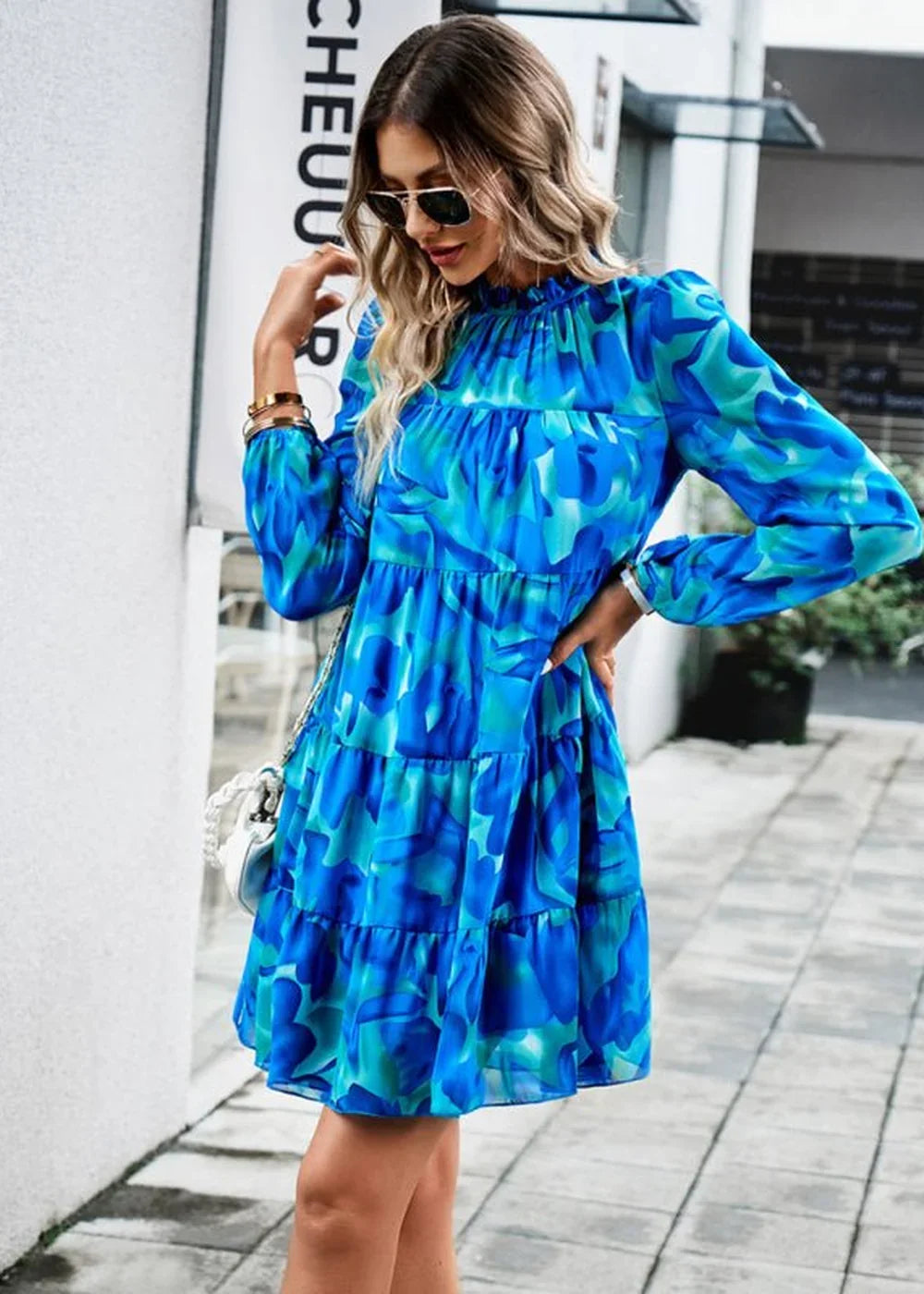 Blue and green abstract floral print tiered mini dress with long sleeves and mock neck on model.