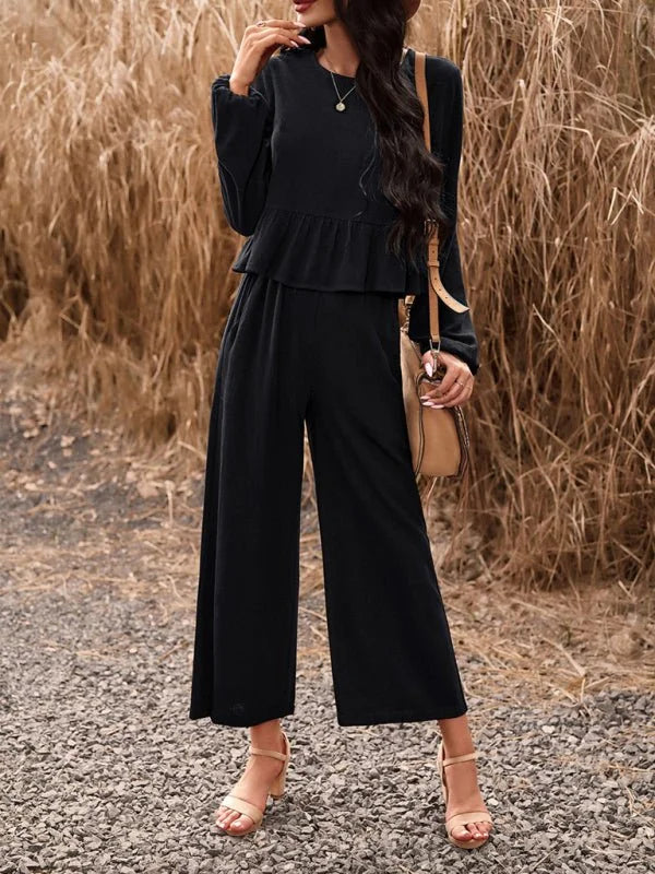 Black wide-leg pant suit with ruffled peplum top and tan sandals on model.