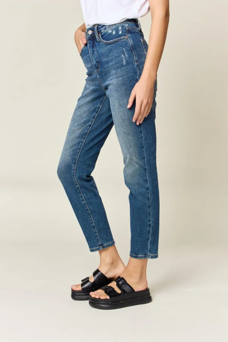 Distressed medium-wash denim jeans with a relaxed fit and frayed hem, shown on a model with black platform slides.