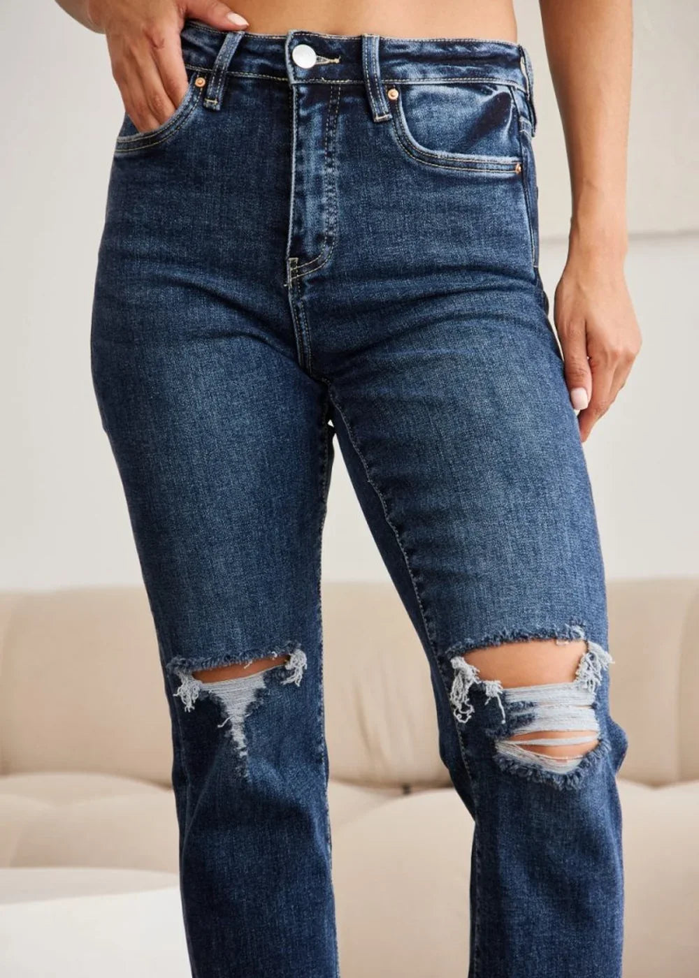 Close-up of dark wash ripped jeans with frayed hems on a model.