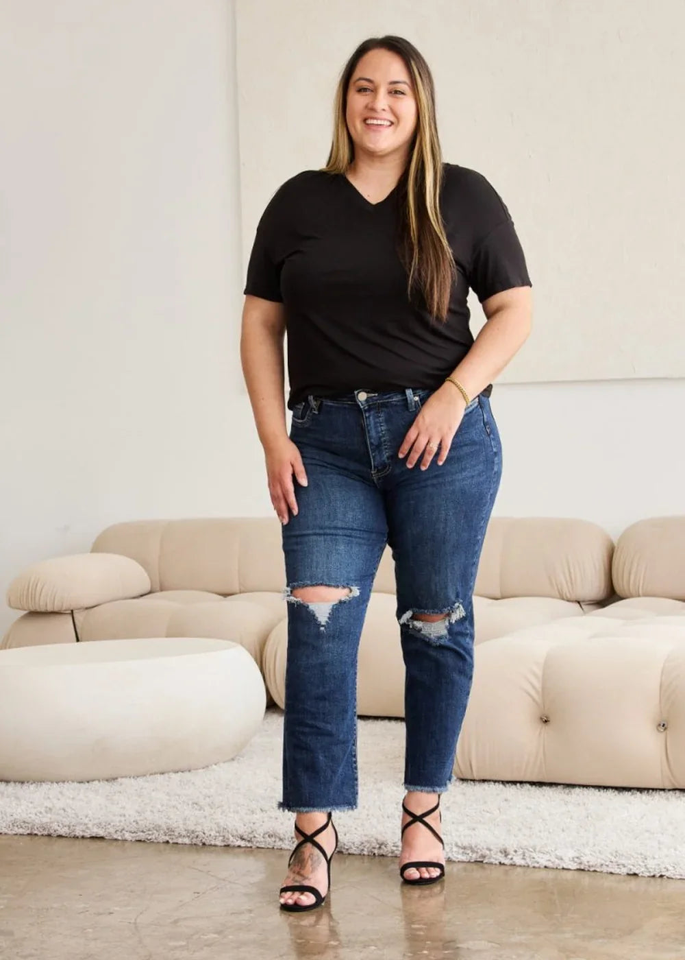 Dark wash distressed denim jeans with a frayed hem and v-neck black t-shirt on a model.