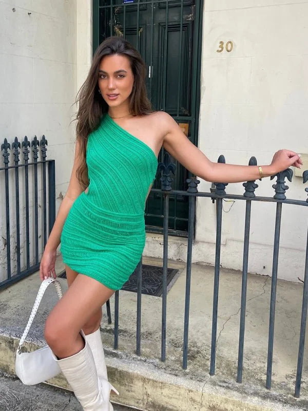 Green one-shoulder knit mini dress with cutout detail, paired with white boots and bag.