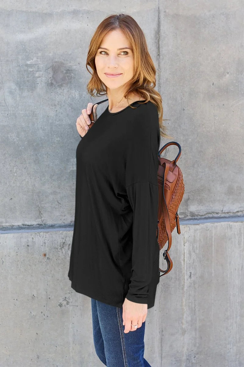 Woman wearing a black long-sleeved top and blue jeans, with a brown woven backpack.