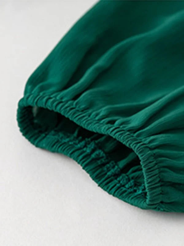 Close-up of a dark emerald green polyester dress sleeve with elasticized cuff and gathered fabric texture.