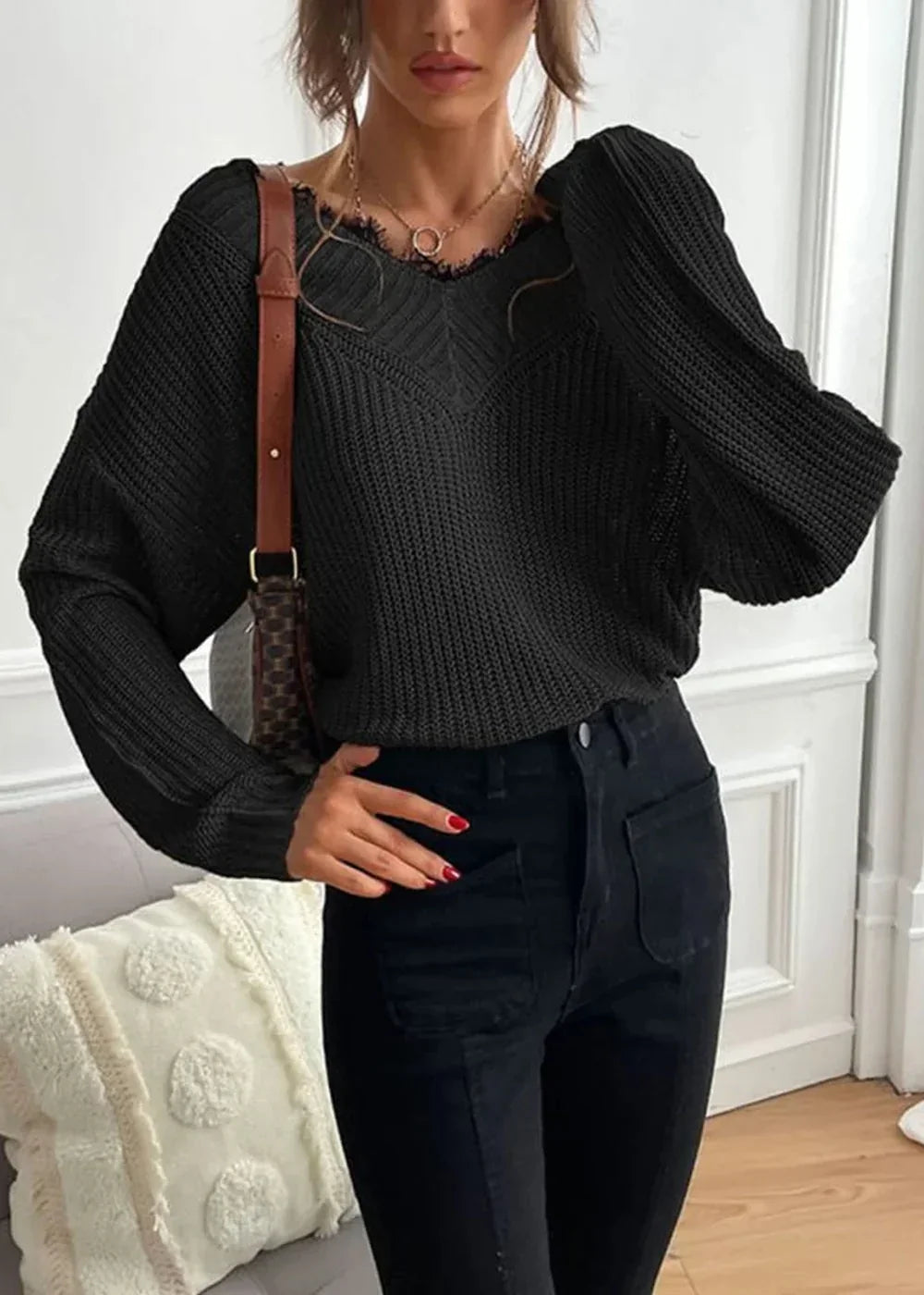 Black knit sweater with frayed V-neck and long sleeves, worn by a model with black jeans.