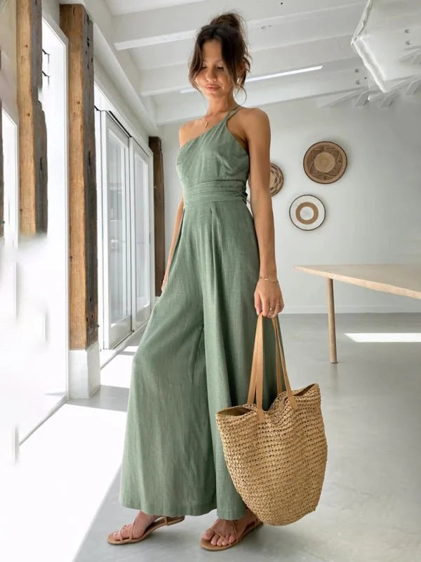 Sage green one-shoulder wide-leg jumpsuit with a woven straw tote bag on a model.