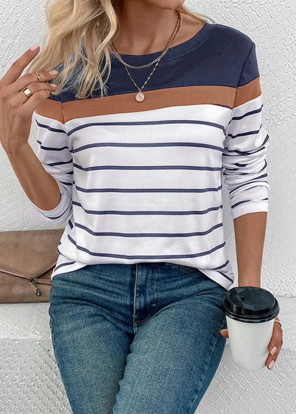 Woman in a navy, brown, and white striped long-sleeve top and blue jeans, holding a coffee cup.