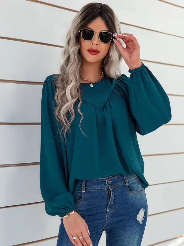 Teal long-sleeve blouse with ruched neckline and gold-tone jewelry on a model wearing distressed blue jeans.