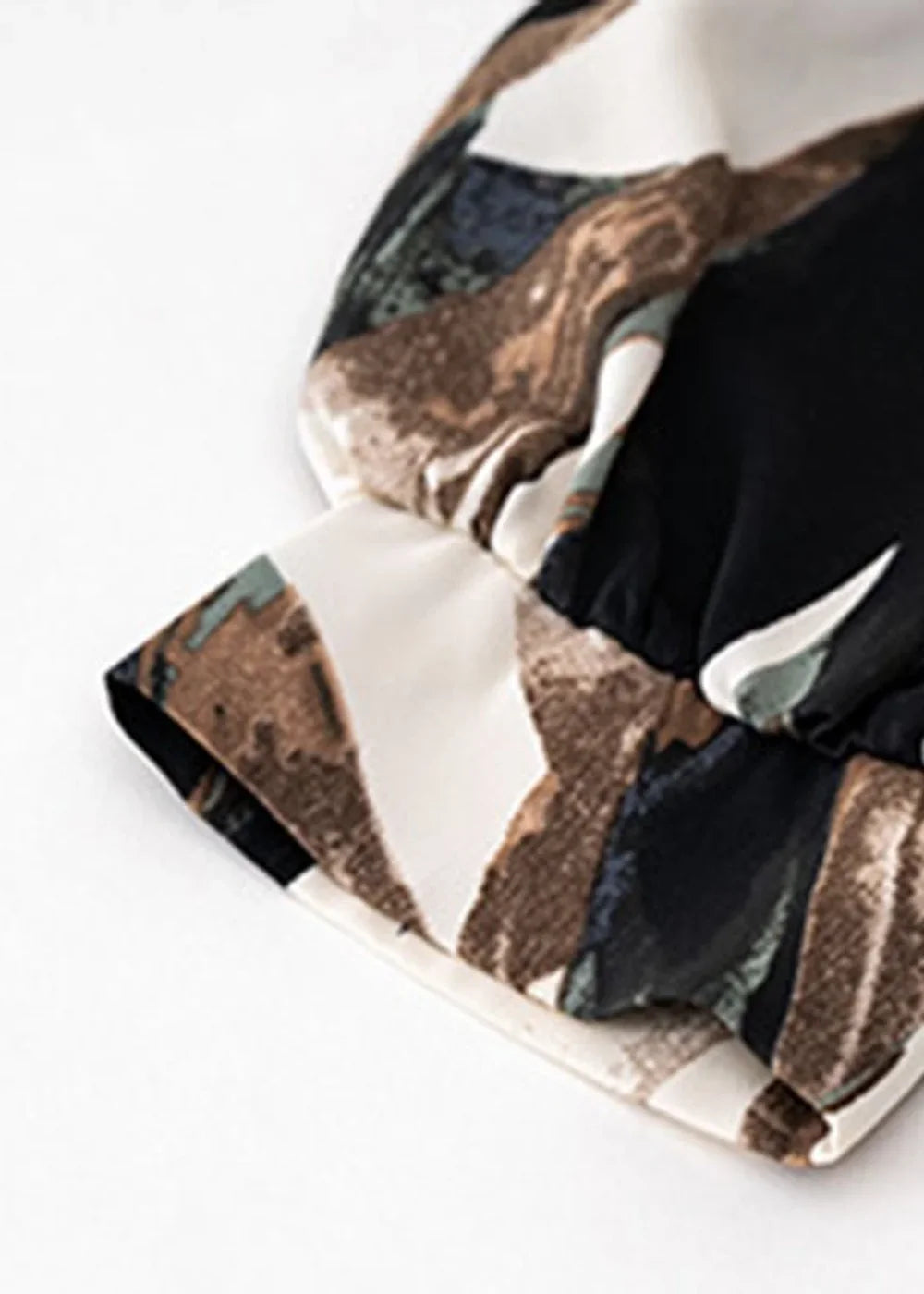 Close-up of a white sleeve cuff with a brown, black, and green abstract print.