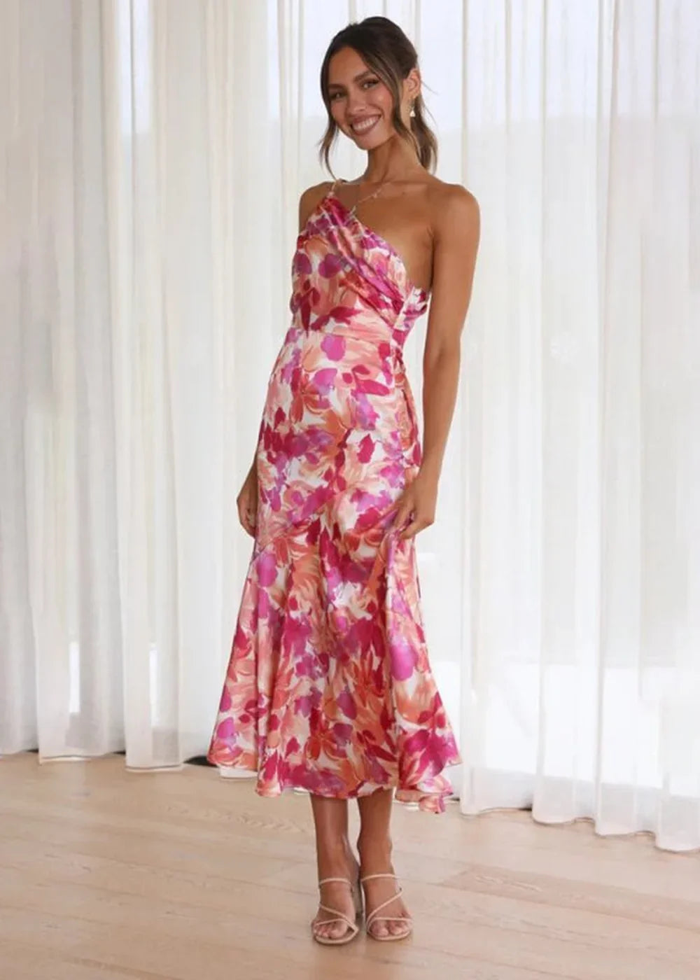 Woman in a one-shoulder floral print midi dress in shades of pink, orange, and white.