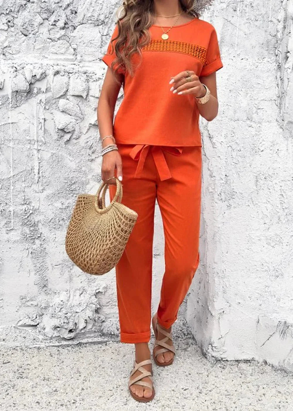 Orange linen-blend pant suit with a tie-waist and straw tote bag.