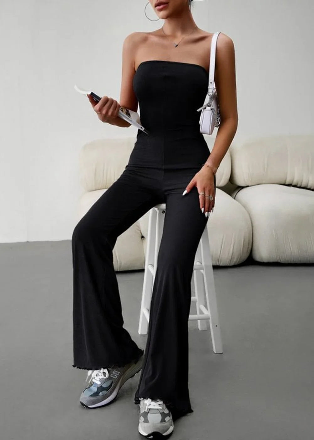 Black strapless flared jumpsuit with frayed hem, worn by a model on a stool.