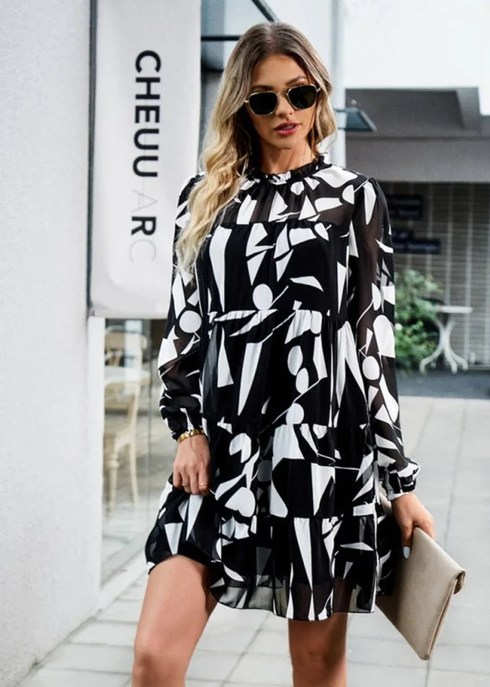 Black and white abstract print chiffon tiered dress with long sleeves and a high neckline on a model.
