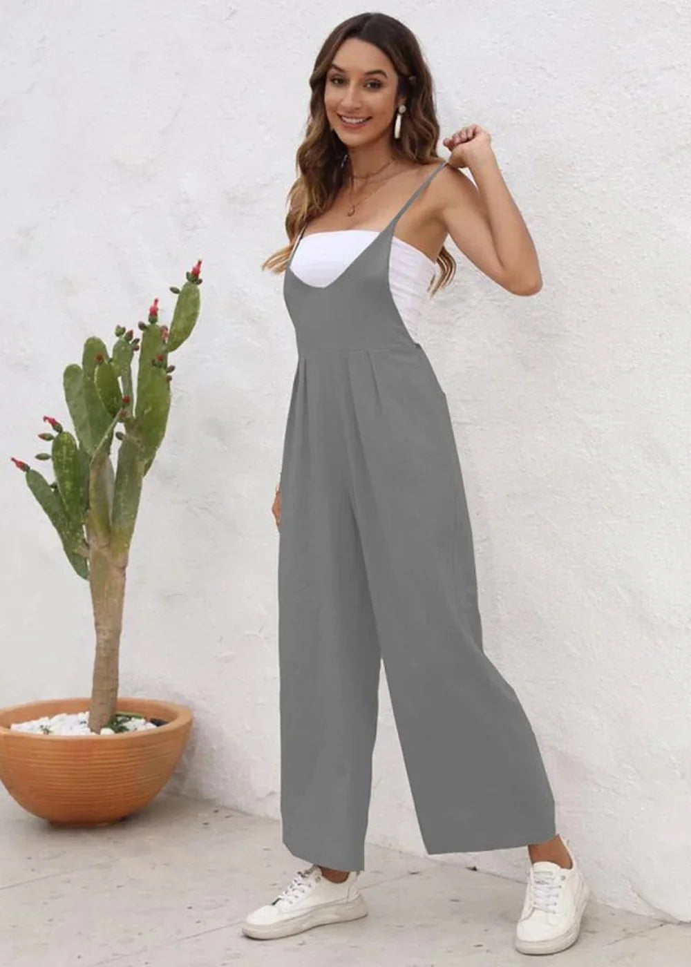 Woman in grey wide-leg jumpsuit and white top, standing next to a potted cactus.
