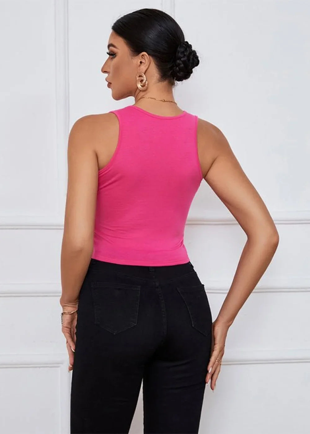 Woman from behind wearing a bright pink sleeveless cropped top and black skinny jeans.