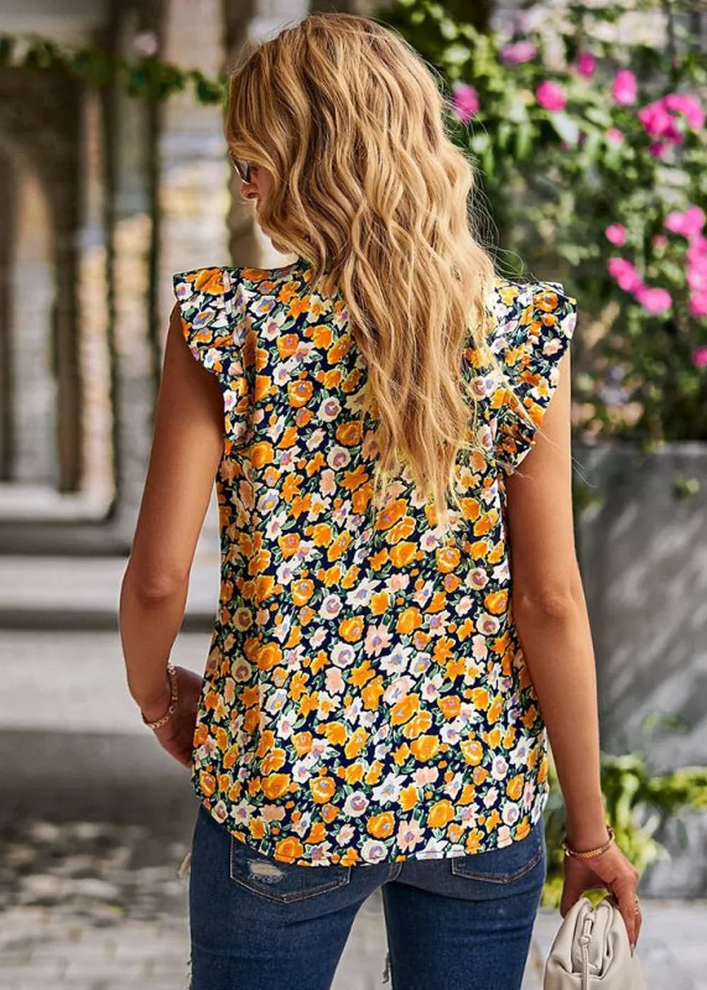 Back view of a woman wearing a navy blue top with a vibrant yellow, orange, and pink floral print and ruffled sleeves.