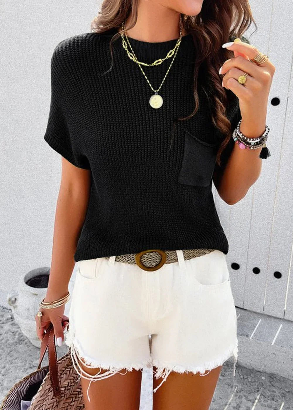 Black knit short-sleeve top with a chest pocket, paired with white frayed shorts and layered gold necklaces.