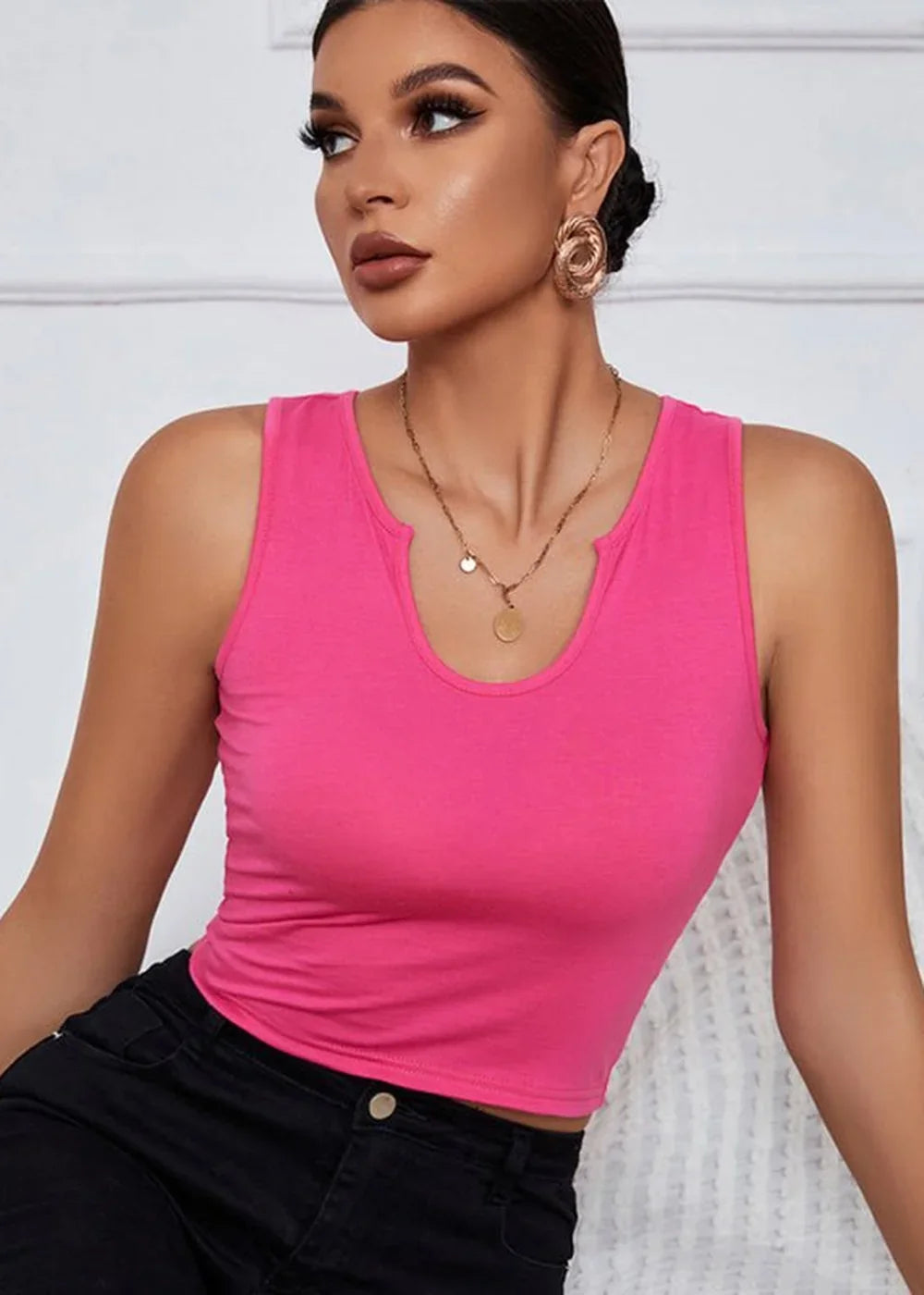 Hot pink cropped tank top with a notched neckline on a woman wearing black pants and gold earrings.