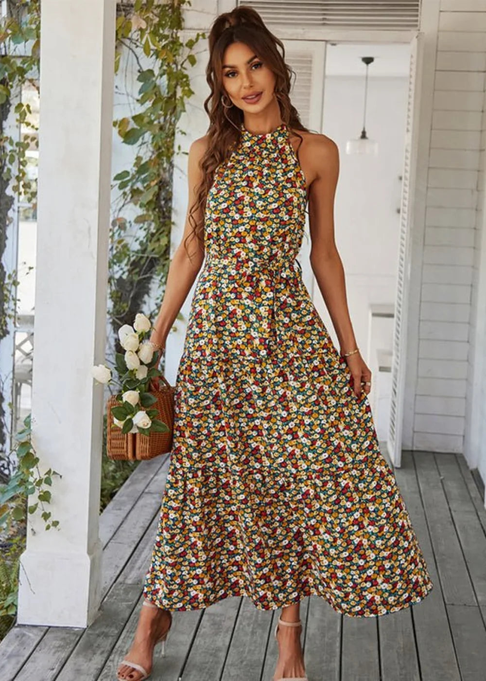 Woman in a floral print maxi dress with a halter neck and tiered skirt, holding a basket of white roses.