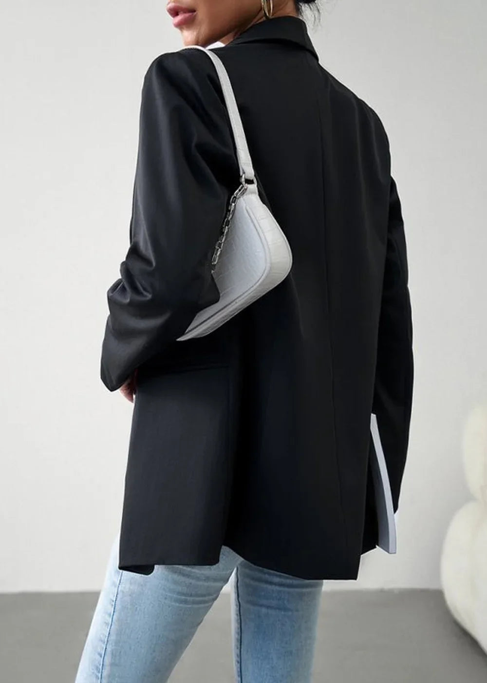 Black oversized blazer with a light grey textured shoulder bag and light wash denim jeans.