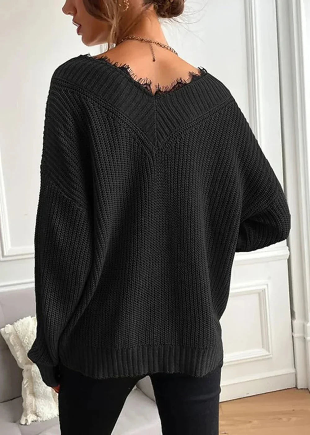 Black distressed knit sweater with V-neck and frayed hem, shown from the back on a model.