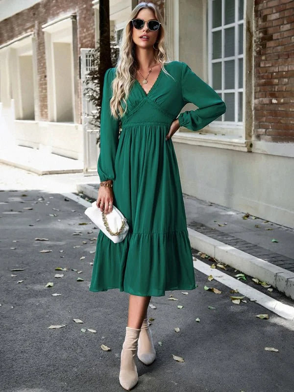 Emerald green midi dress with V-neck, tiered skirt, and long sleeves, held by a woman wearing light beige boots.