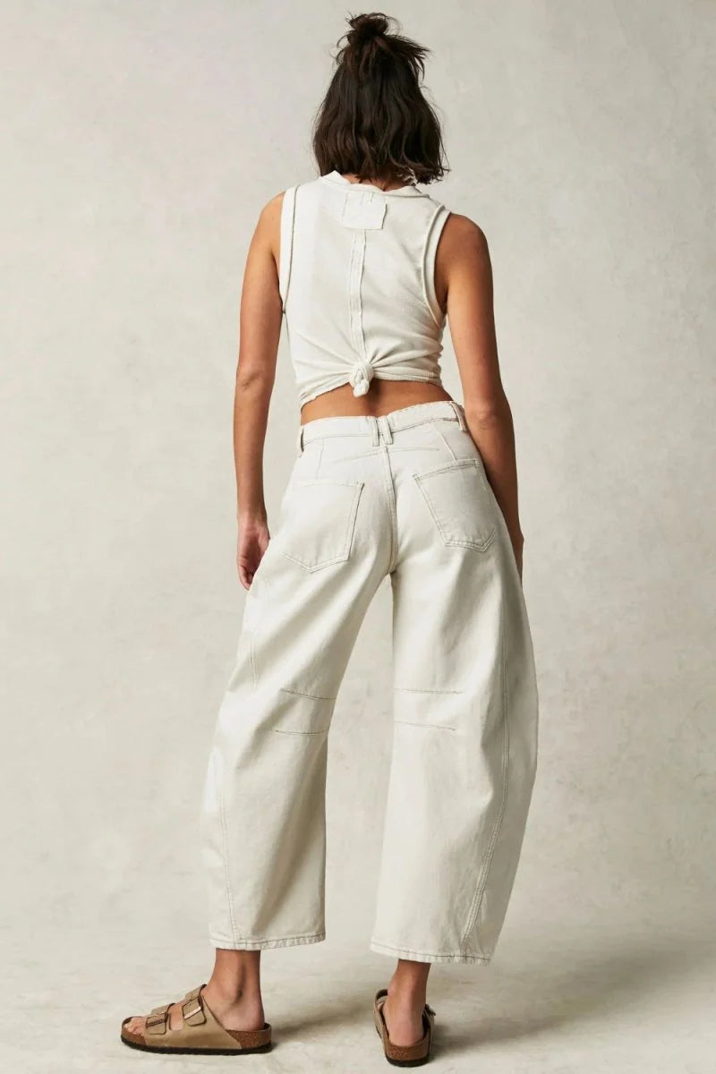 Back view of woman in relaxed-fit, cream-colored denim pants with a knotted white tank top.