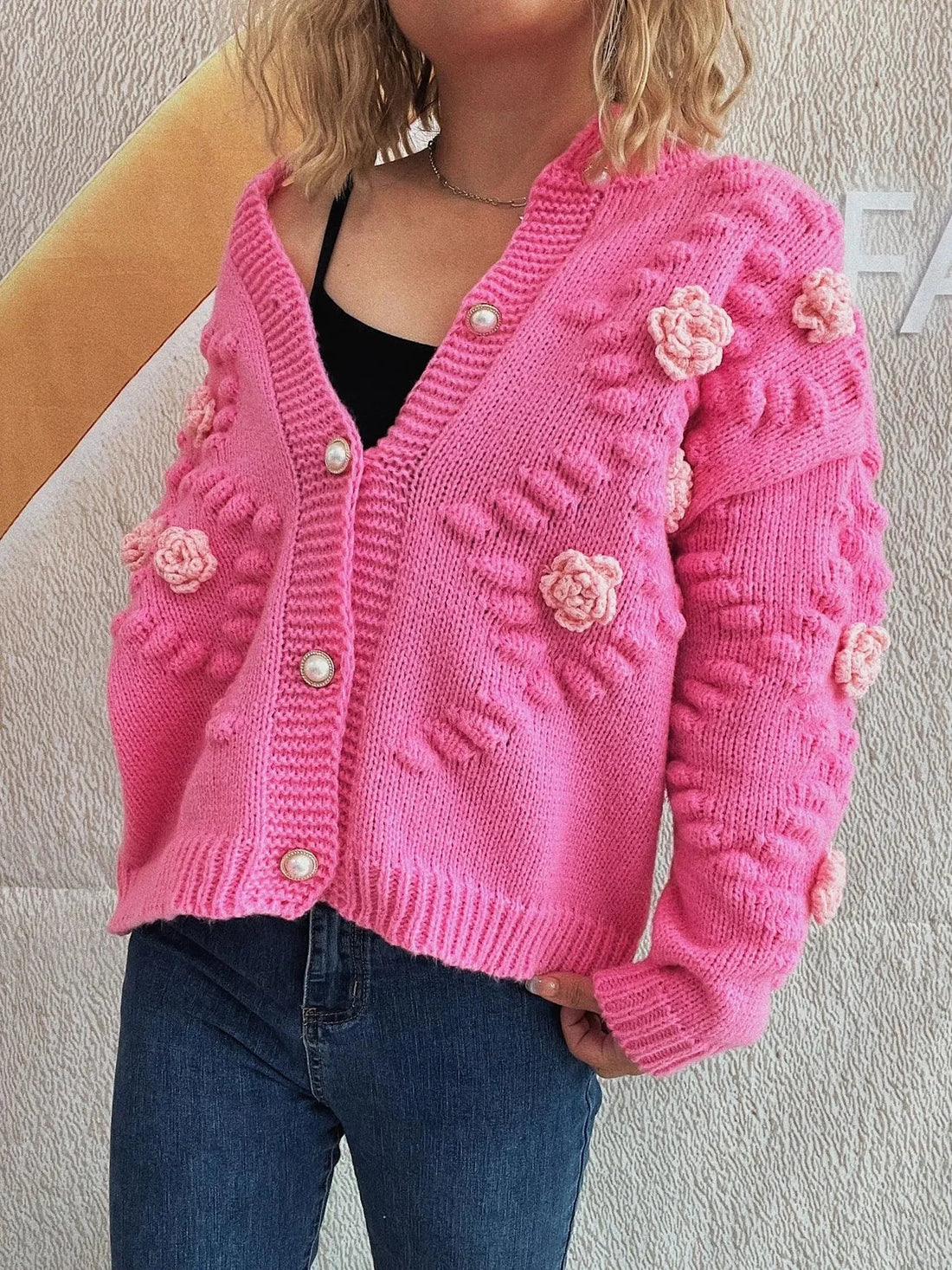 Pink knit cardigan with floral appliques and pearl buttons, worn by a model.