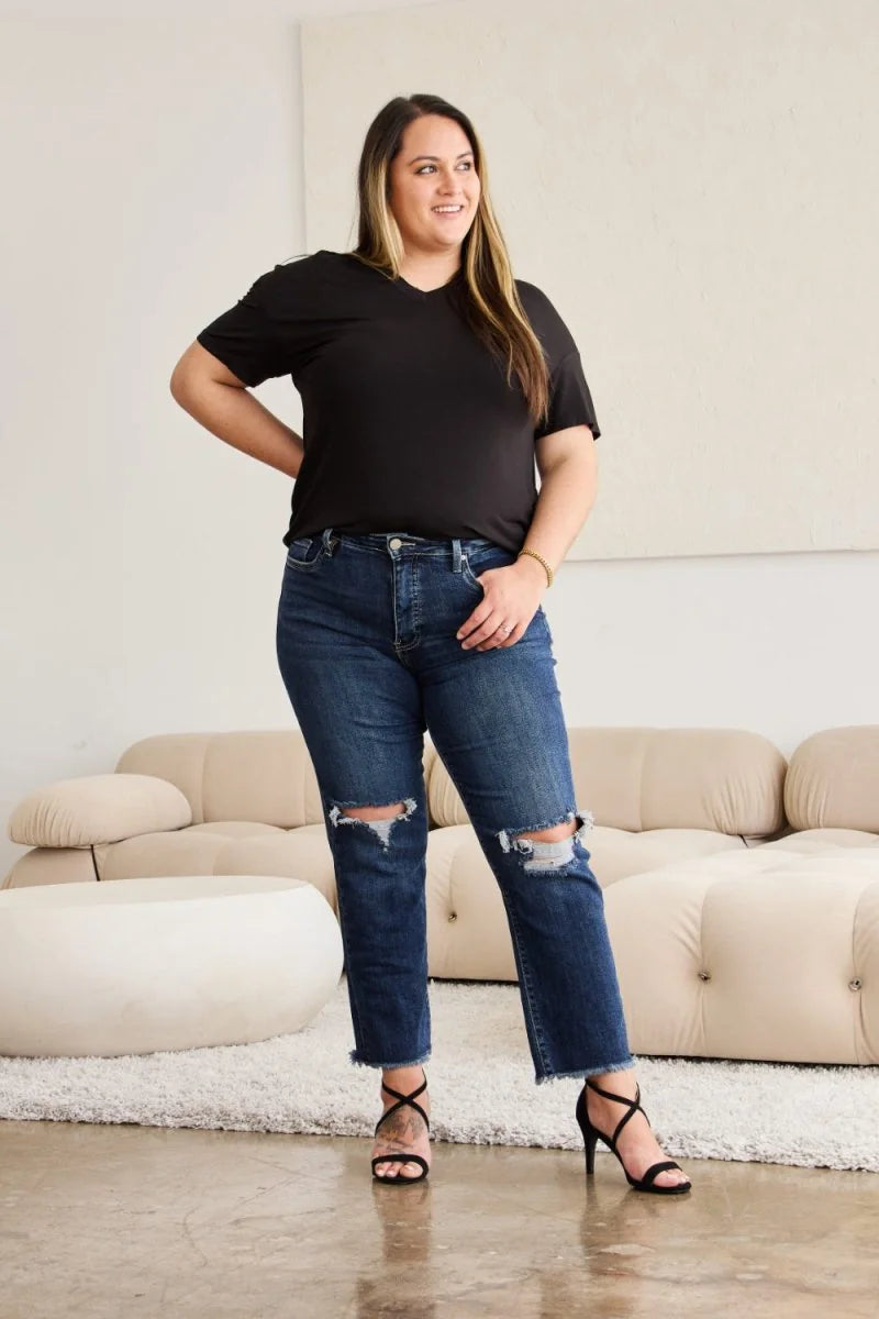 Woman in dark wash distressed denim jeans with frayed hems and black strappy heels.