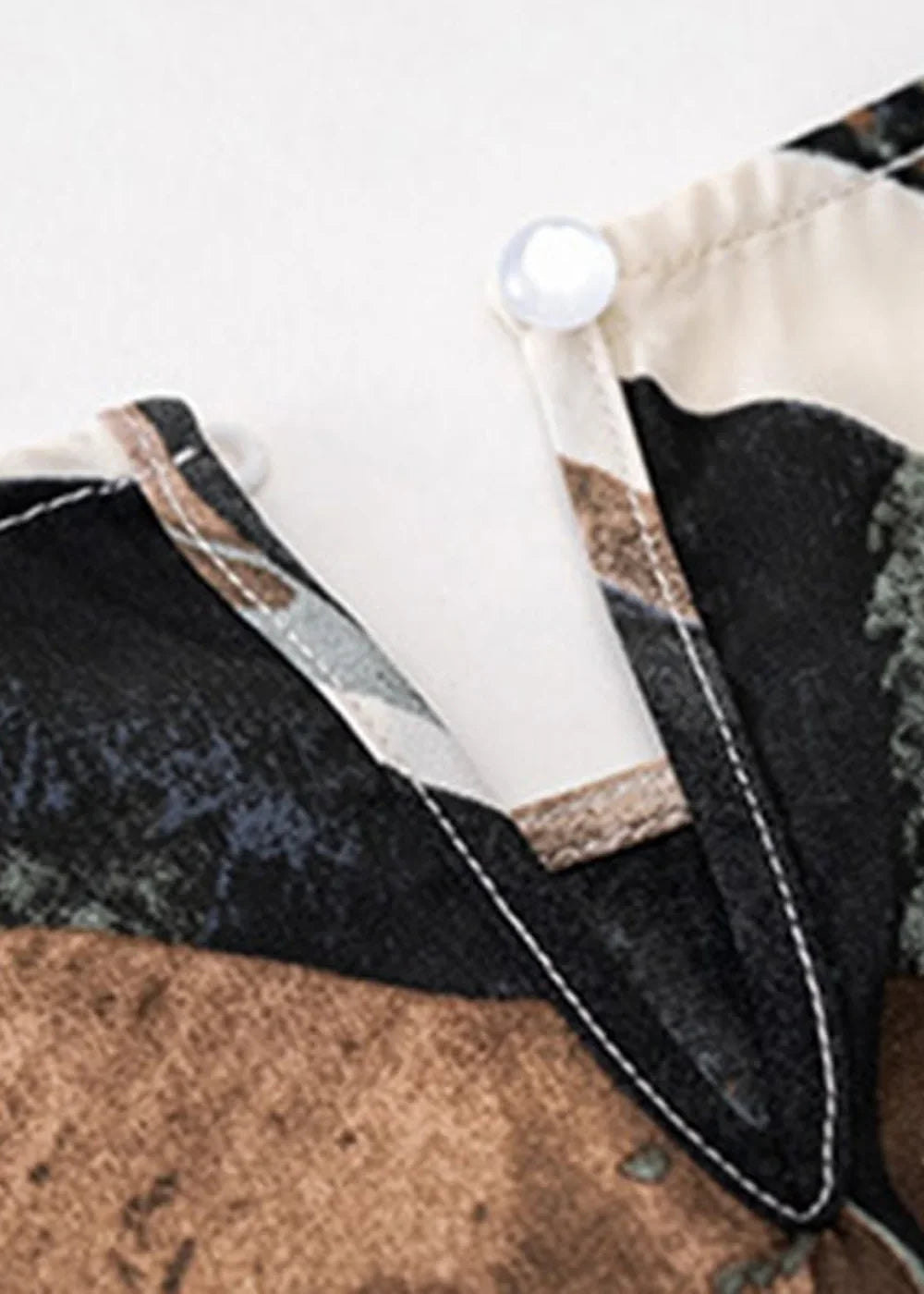 Close-up of a cream and black print collar with a pearl button closure on a pant suit.