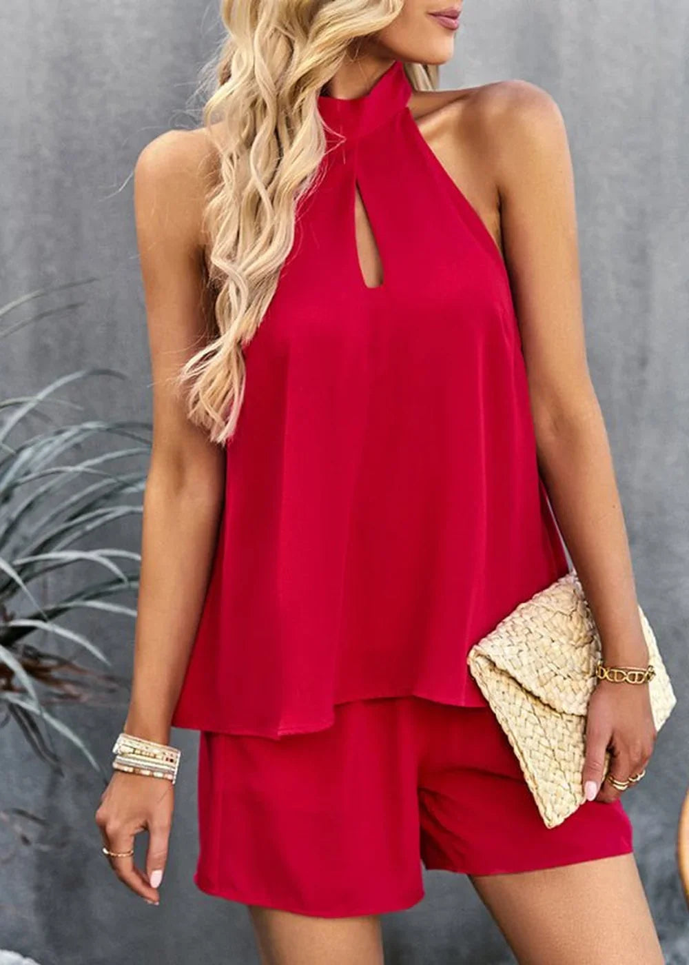 Red halterneck sleeveless top with cutout detail and matching shorts, worn by a model with blonde hair and a straw clutch.