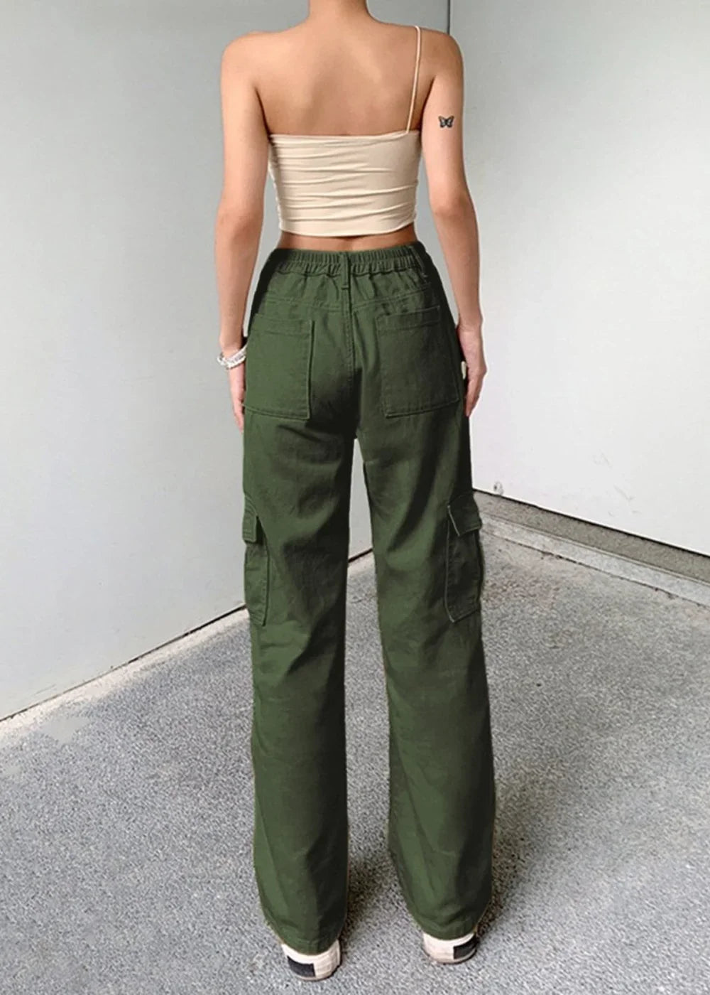 Back view of woman in olive green cargo pants and beige spaghetti strap crop top.