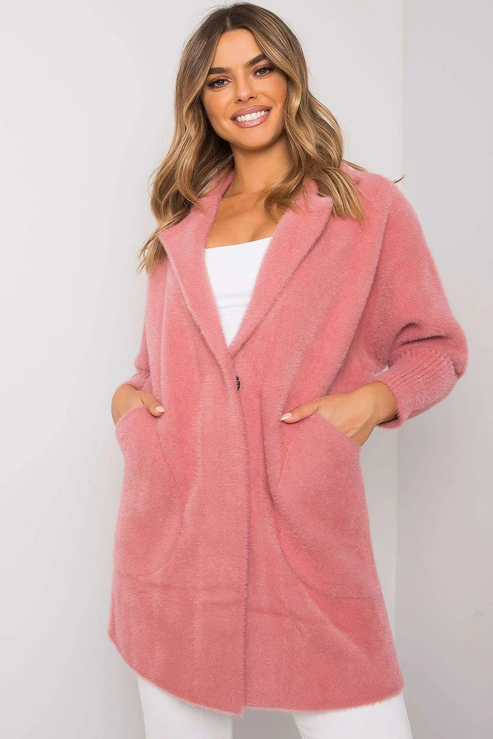 A woman wears a fuzzy pink angora wool blend coat with pockets and a single button closure.
