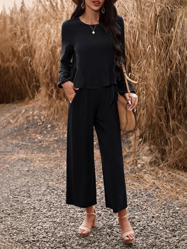 Black wide-leg pant suit with ruffled waist detail, worn by a model with nude block heel sandals.