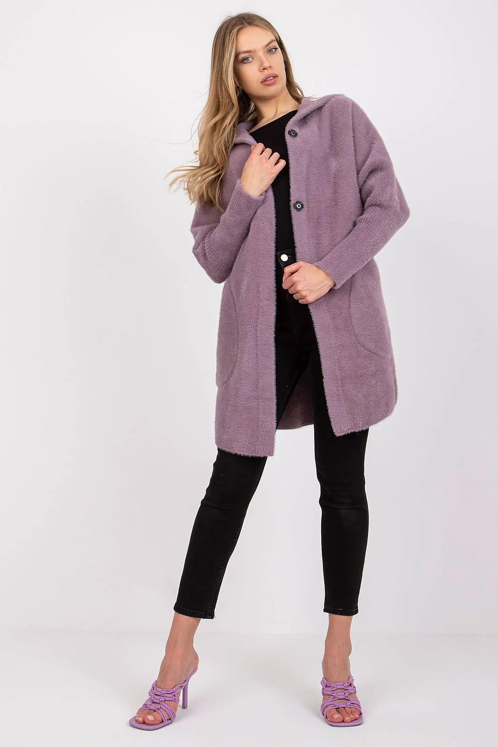 Woman in a long, fuzzy, lavender hooded cardigan with two black buttons and black pants.