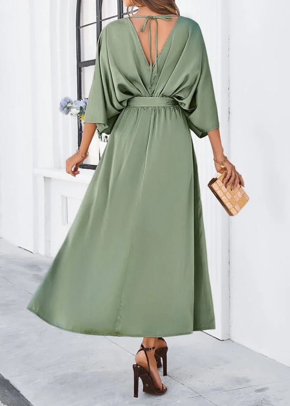 Sage green satin maxi dress with V-neck and tie detail, worn by a model holding a gold clutch.