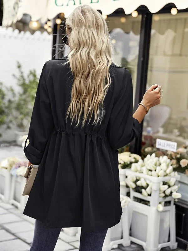 Black cinched-waist trench coat with rolled sleeves, worn by a model from behind.