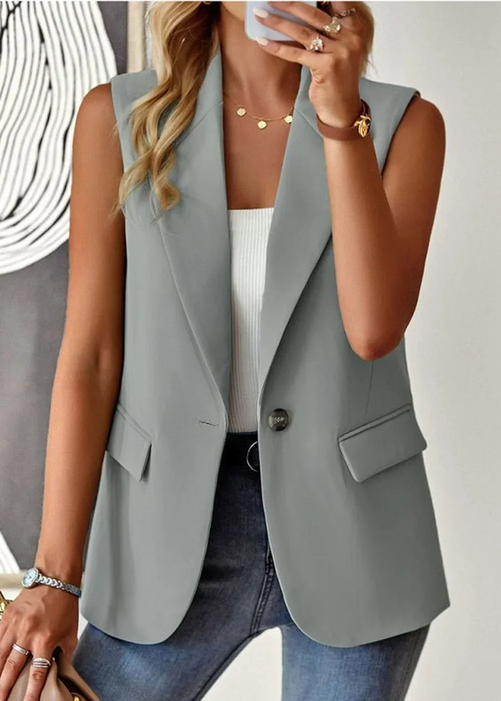 Light gray sleeveless blazer with a single button closure, welt pockets, and a white ribbed tank top worn by a model.