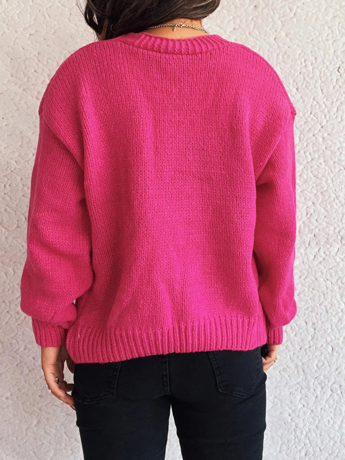 Woman in a bright pink, textured knit sweater with black jeans.