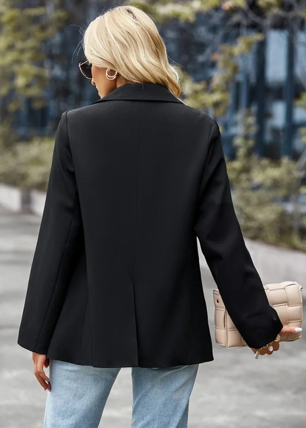 Back view of a woman wearing a black blazer and light blue jeans, holding a beige woven purse.