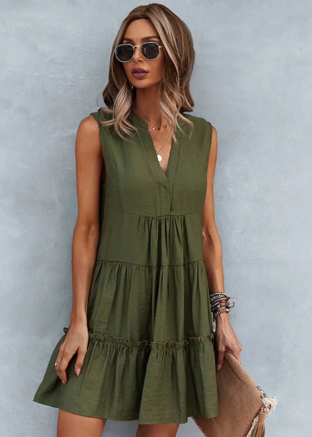 Olive green tiered sleeveless V-neck dress with ruffled hem, worn by a model with sunglasses and a clutch.