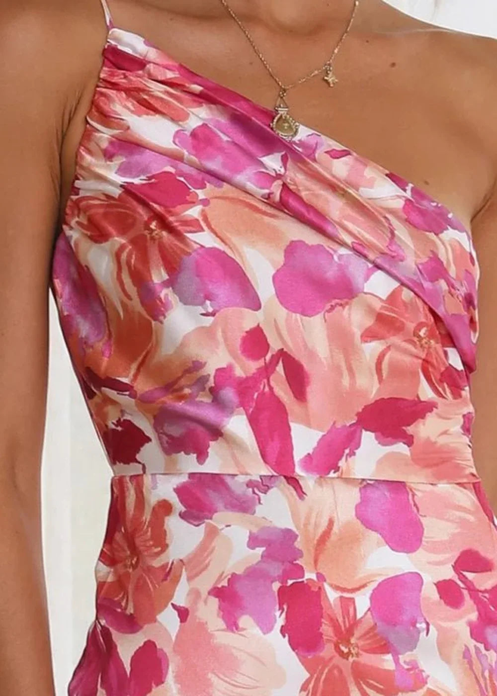 Close-up of a satin dress with a vibrant pink and orange floral print, featuring a one-shoulder design.