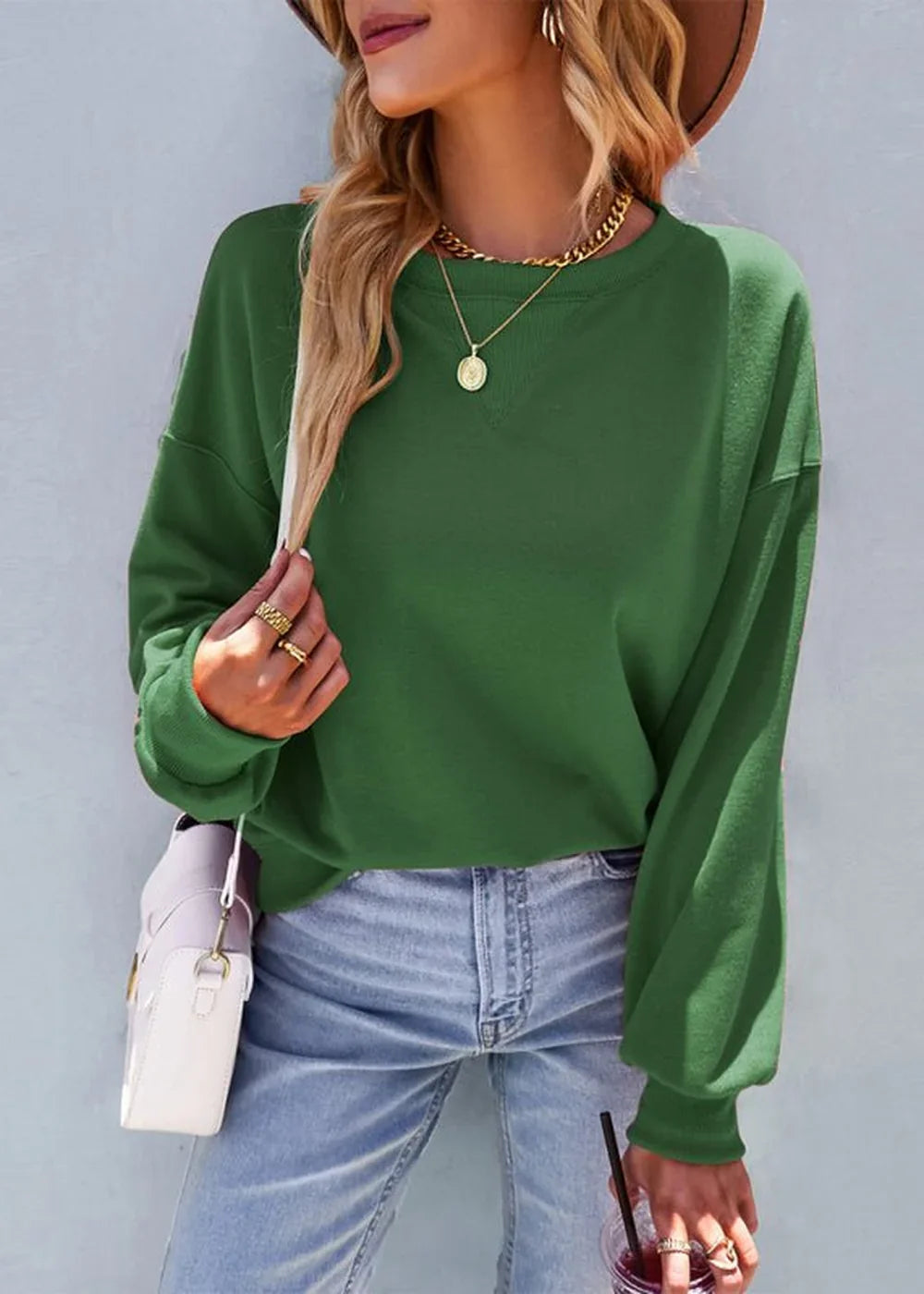 Loose-fit green crew neck sweatshirt with balloon sleeves, worn with light wash jeans and gold jewelry.