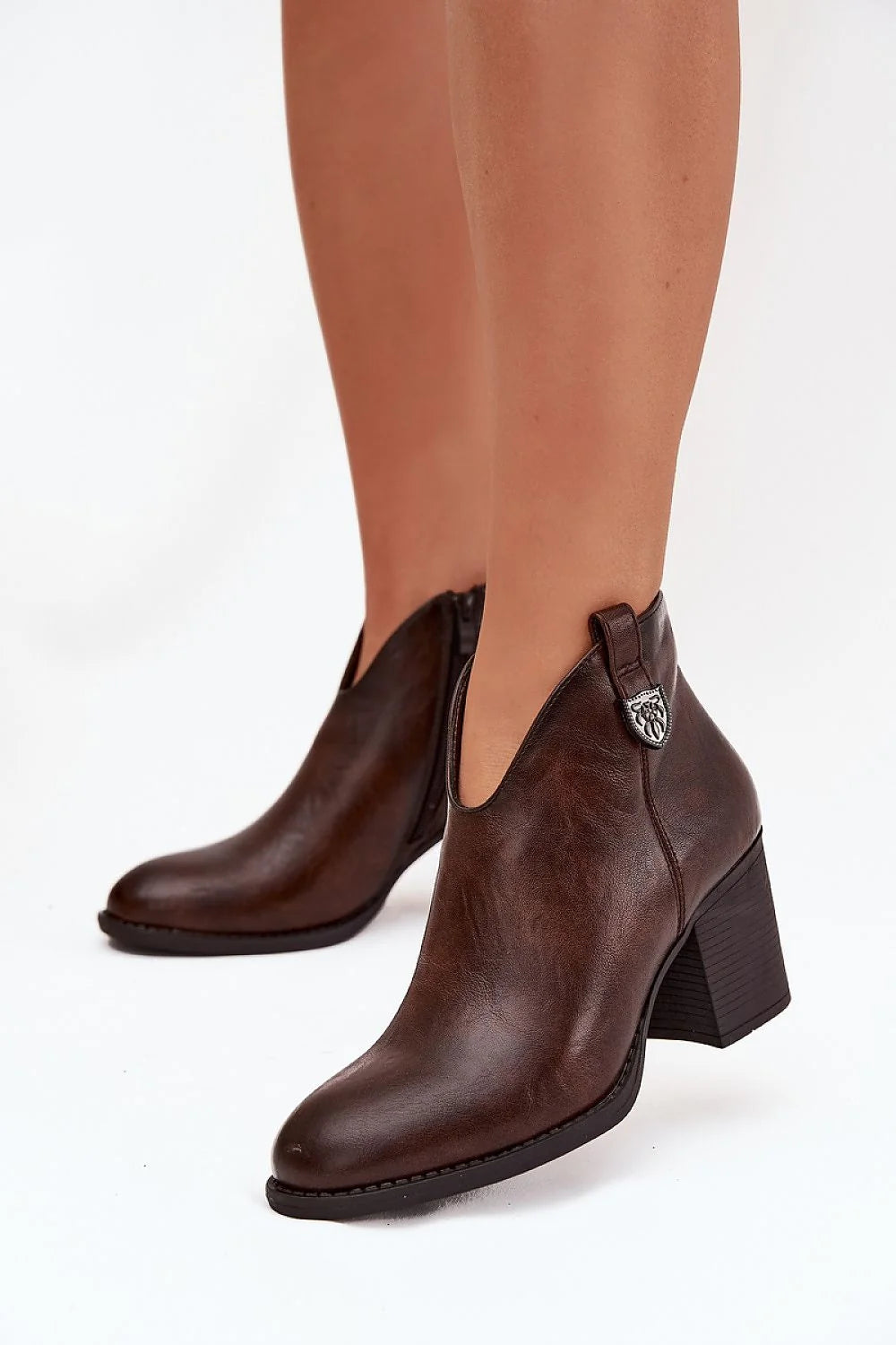 Brown leather ankle boots with a pointed toe and block heel, featuring a decorative silver emblem.
