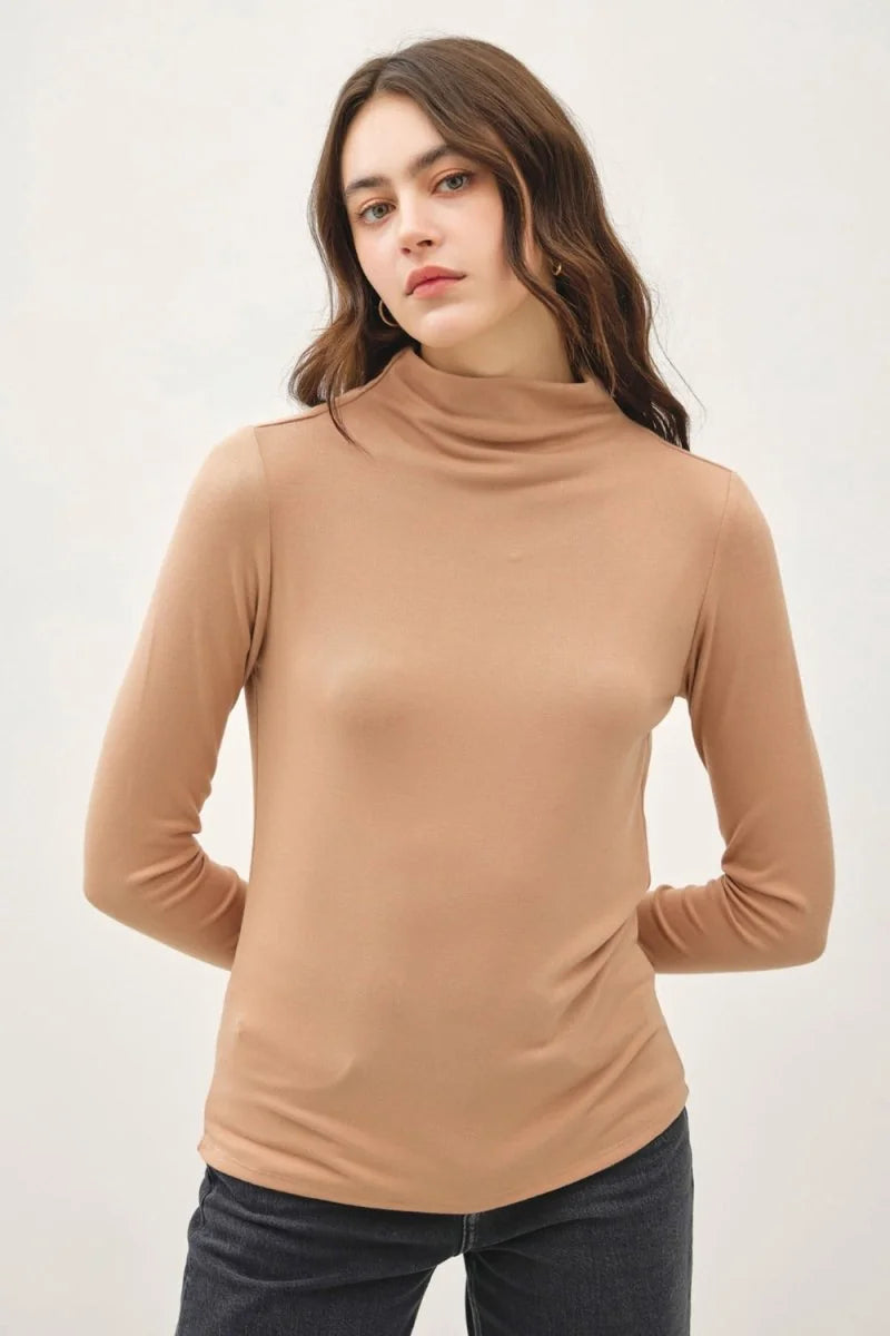Woman in a long-sleeved camel turtleneck top with a smooth, slightly sheer texture, tucked into dark wash jeans.