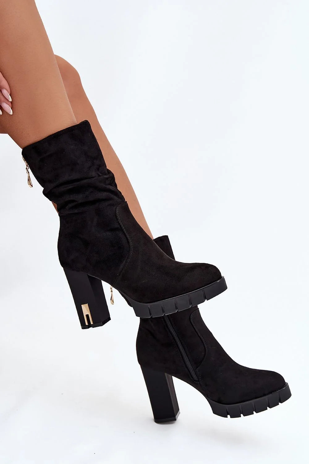 Black suede slouch boots with chunky heel and gold zipper detail on model.